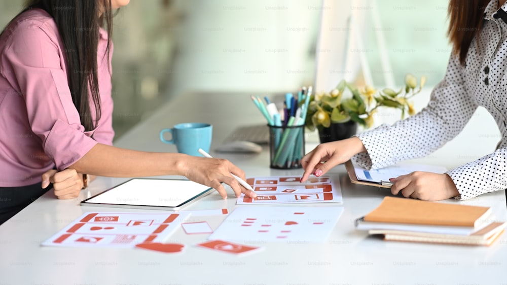 Cropped shot of ux designers are planning interface of mobile website with layouts on table.