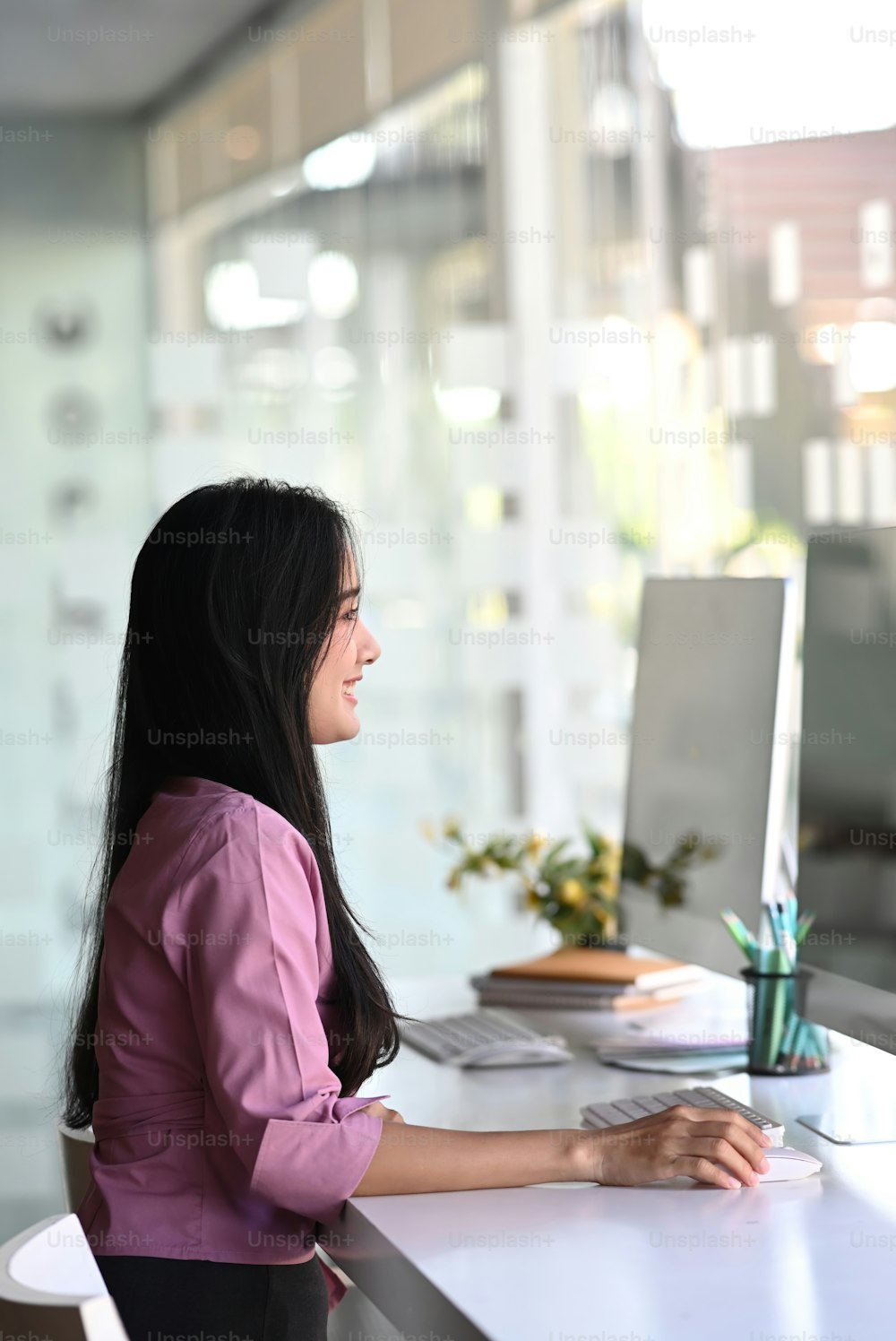 Retrato de una joven empresaria feliz sentada en la silla de la oficina trabajando en la computadora en el lugar de trabajo moderno del distrito de negocios.
