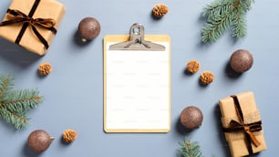 Mesa de trabajo festiva con portapapeles en blanco, cajas de regalo, ramas de abeto, bolas sobre fondo azul pastel. Navidad, concepto de vacaciones de invierno. Minimalista, estilo nórdico.