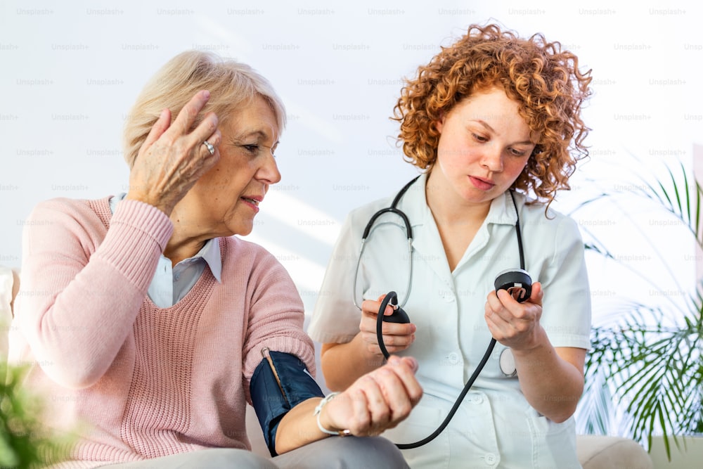 Young nurse measuring blood pressure of elderly woman at home. Female nurse checking blood pressure of a senior woman at home,Home carer checking patients blood pressure
