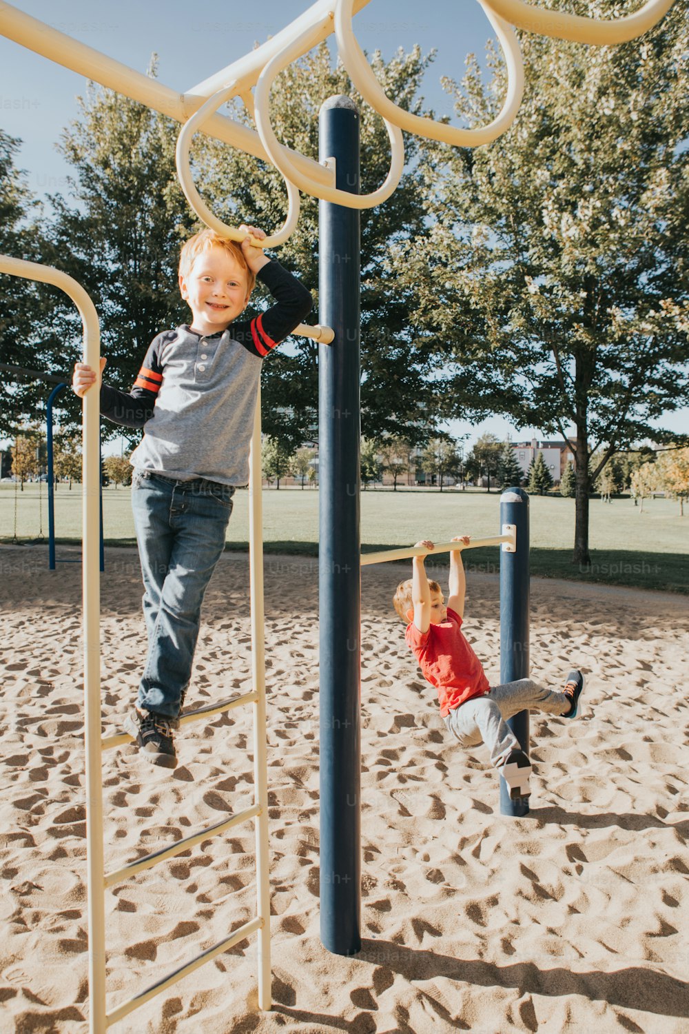 Young Caucasian boys friends hanging on monkey bars and pull-up bars in park on playground. Summer outdoor activity for kids. Active children doing exercises sport. Healthy happy childhood.