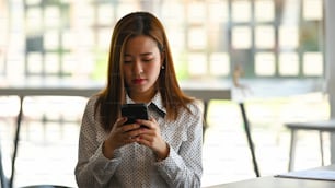 Retrato de una mujer de negocios concentrada en el teléfono móvil y sentada en su lugar de trabajo.