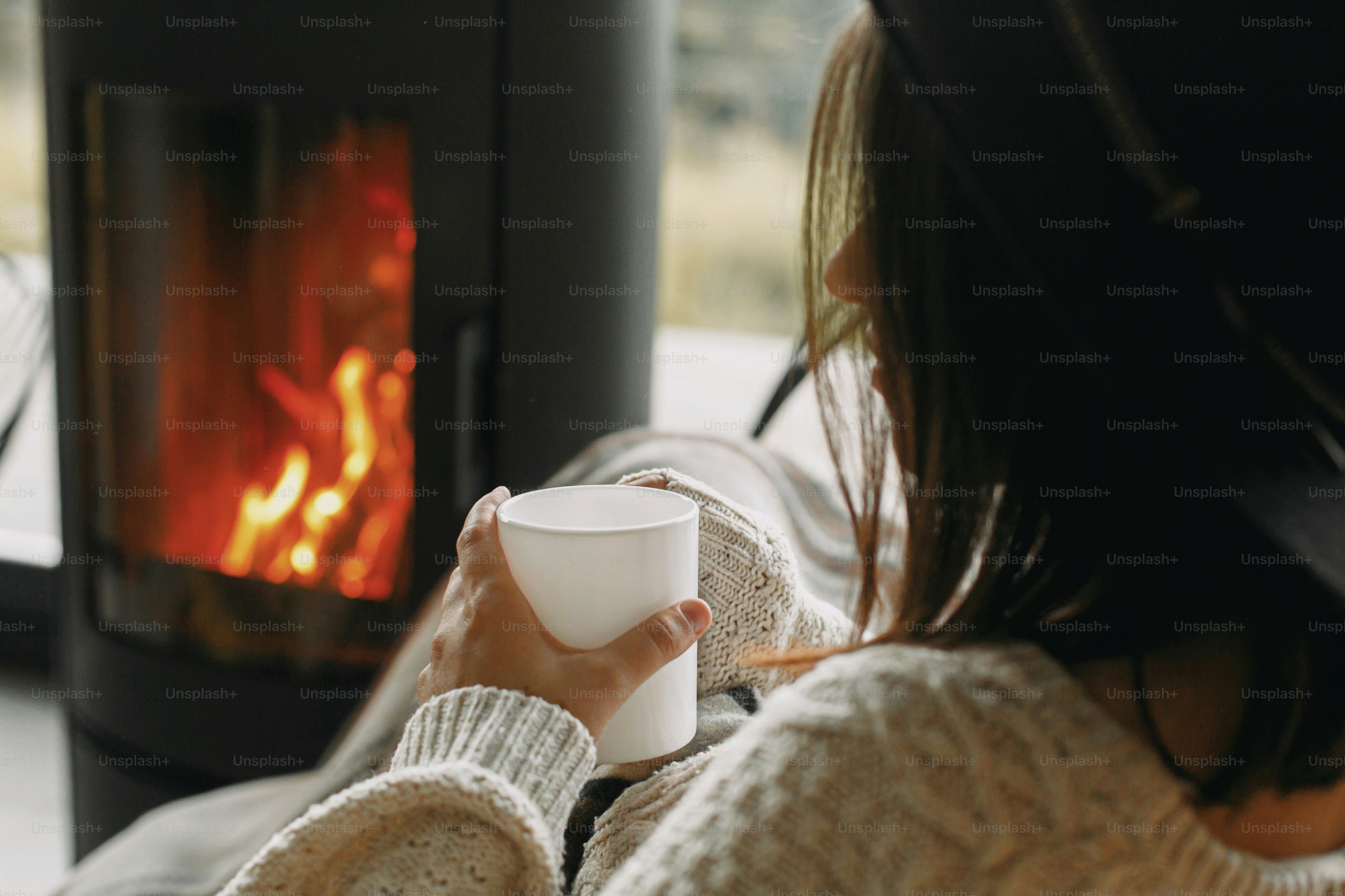 Femme élégante en pull tricoté se relaxant avec une tasse de thé chaud au coin du feu noir moderne avec vue sur les montagnes. Des moments chaleureux et douillets à la saison froide. Jeune femelle au repos