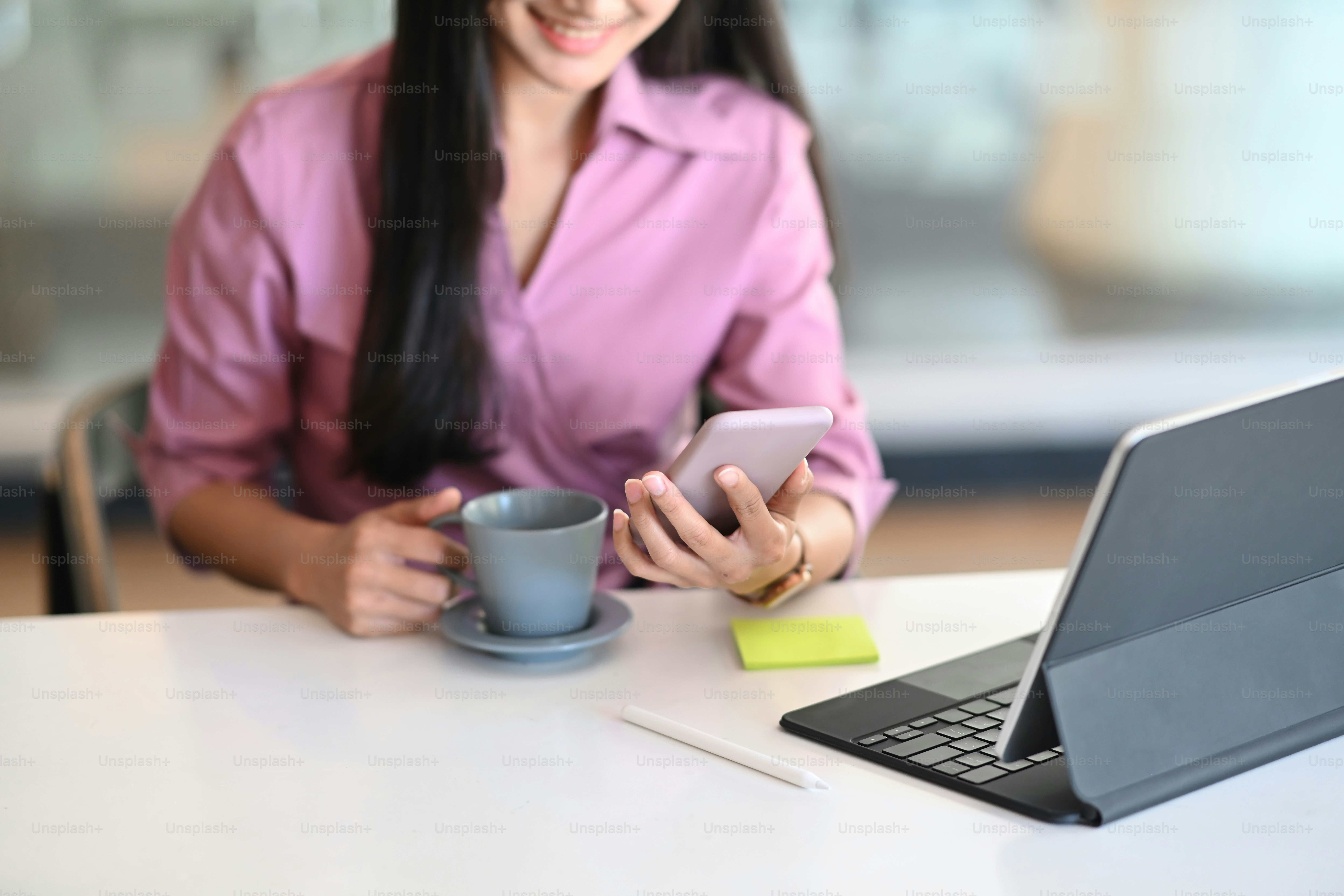 Una mujer joven y hermosa y feliz está usando un teléfono móvil para enviar mensajes de texto en una oficina moderna.
