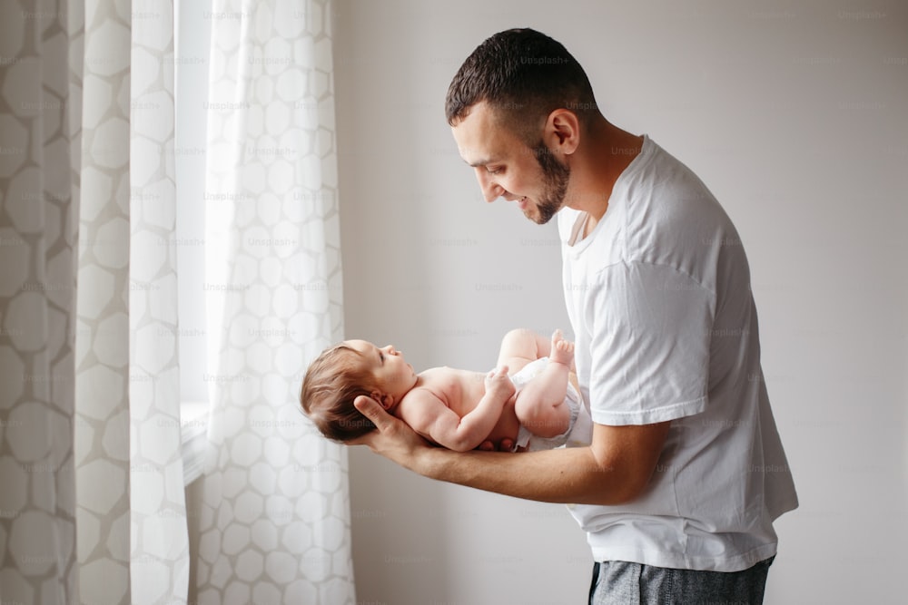 Happy Caucasian father holding newborn baby. Male bearded man parent rocking child daughter son on his hands. Authentic lifestyle candid moment. Young dad family life concept.