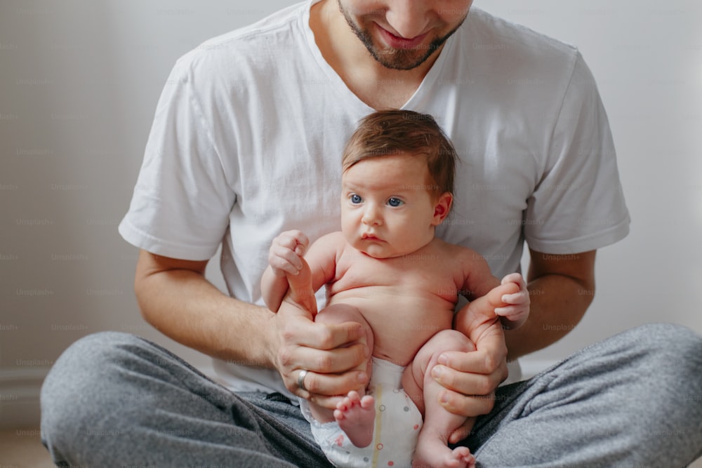 Happy Caucasian father holding newborn baby on laps knees. Man parent embracing rocking child daughter son. Authentic lifestyle candid moment. Proud young dad. Family fathers day.