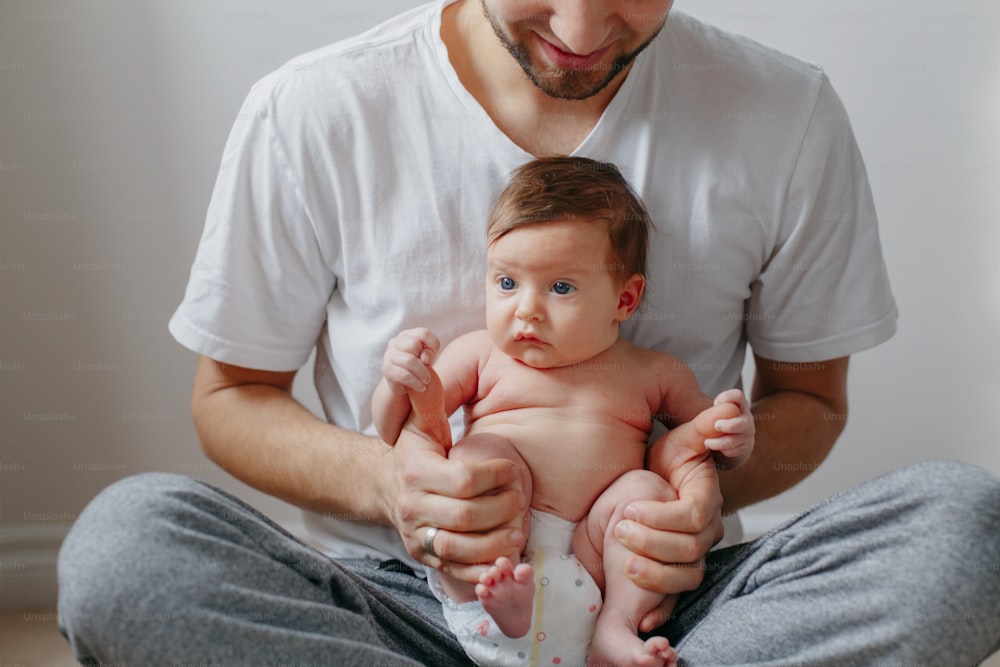 Père caucasien heureux tenant un nouveau-né sur les genoux des genoux. Homme, parent, embrassant, berçant, enfant, fille, fils. Moment authentique de vie candide. Fier jeune papa. Fête des pères en famille.
