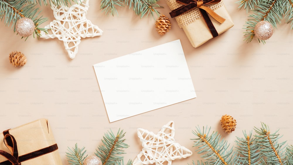 パステル ベージュの背景にクリスマス グリーティング カードのモックアップ、ギフト ボックス、星、ボール、装飾、モミの木の枝。フラットレイ、上面図。ミニマルなスタイル。