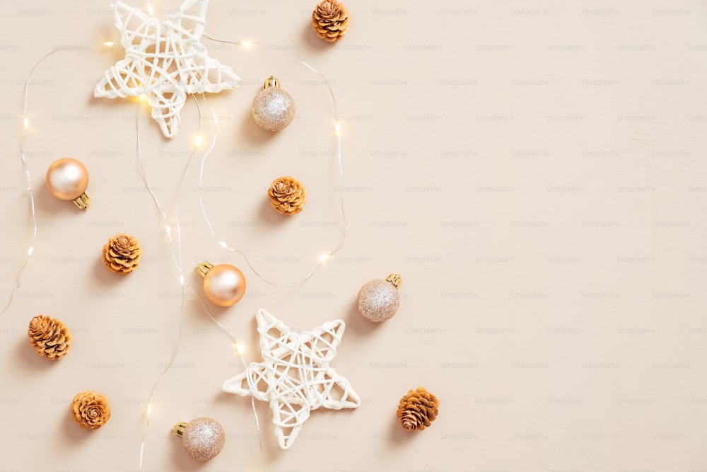 Elegante composición navideña. Decoraciones planas de estrellas, bolas, conos, guirnalda sobre fondo beige pastel. Tarjeta de felicitación de Navidad. Glamour, estilo de moda. Plano tendido.