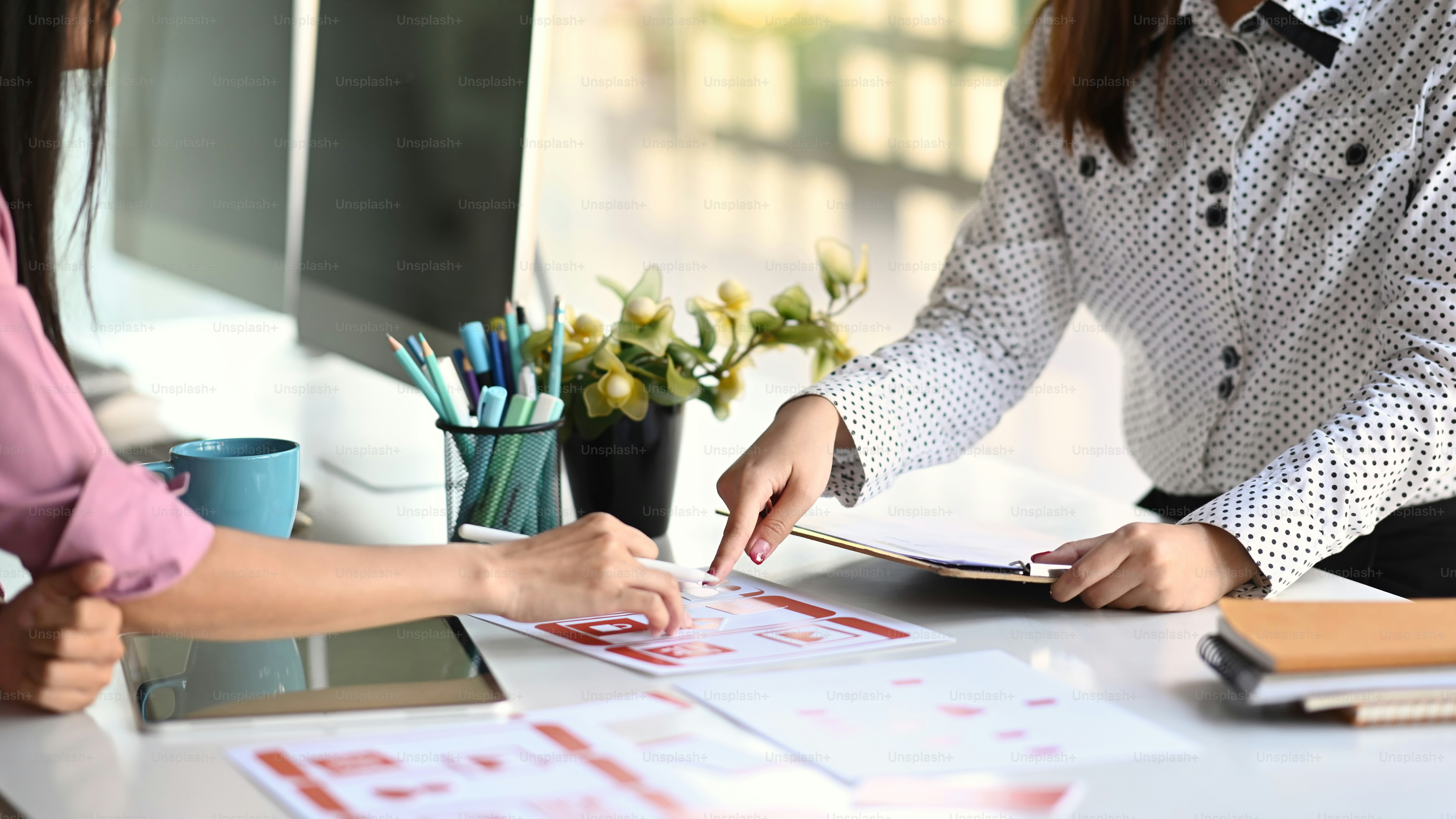 Eine Gruppe asiatischer UI / UX-Entwickler brainstormt über das Wireframe-Design der mobilen App-Schnittstelle auf dem Tisch in einem modernen Büro.