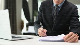 A confident businessman in black suit is writing notes or financial report in modern office.