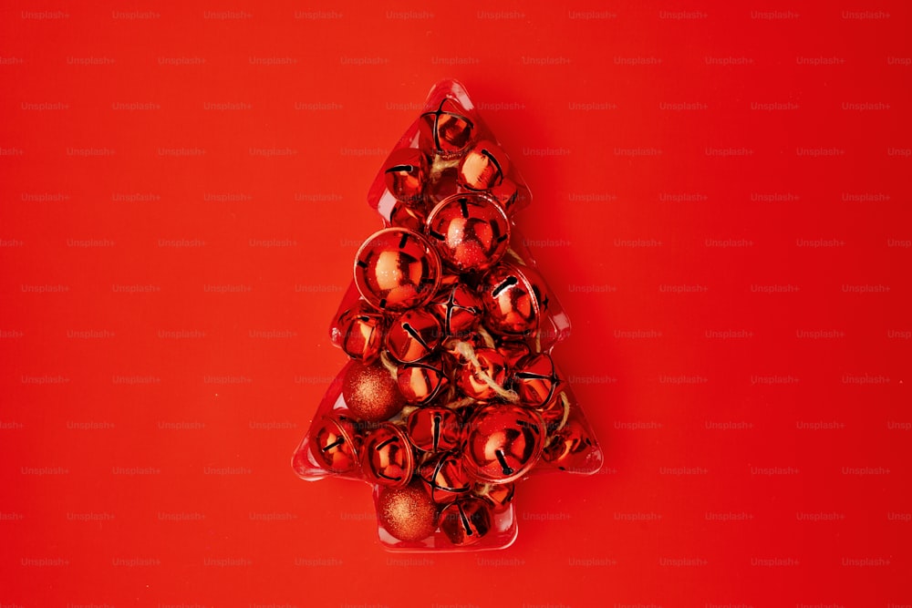 Plano con árbol de Navidad hecho de cascabeles sobre fondo rojo.