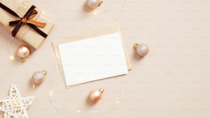 Elegant Christmas composition. Flat lay blank paper card, envelope, garland, Xmas decoration on pastel beige background. Minimal style. Christmas letter concept