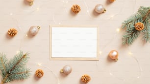 Sobre de carta de Navidad con tarjeta de papel en blanco, adornos dorados, ramas de pino y conos sobre fondo beige pastel. Plano, vista superior.