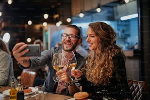 Attraente coppia hipster seduta in un ristorante e scattando un selfie. È l'ora della cena.