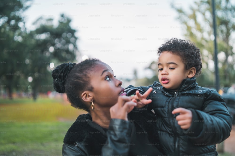 Ritratto di una madre afroamericana con suo figlio in piedi all'aperto nel parco, divertendosi. Famiglia monoparentale.