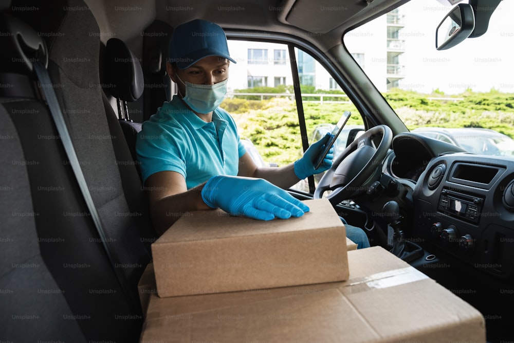 Young courier man in a van is checking packages and waybill using tablet pc before delivery