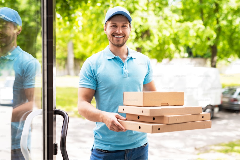 Mensajero sonriente durante la entrega de pizza cerca de una entrada en un edificio