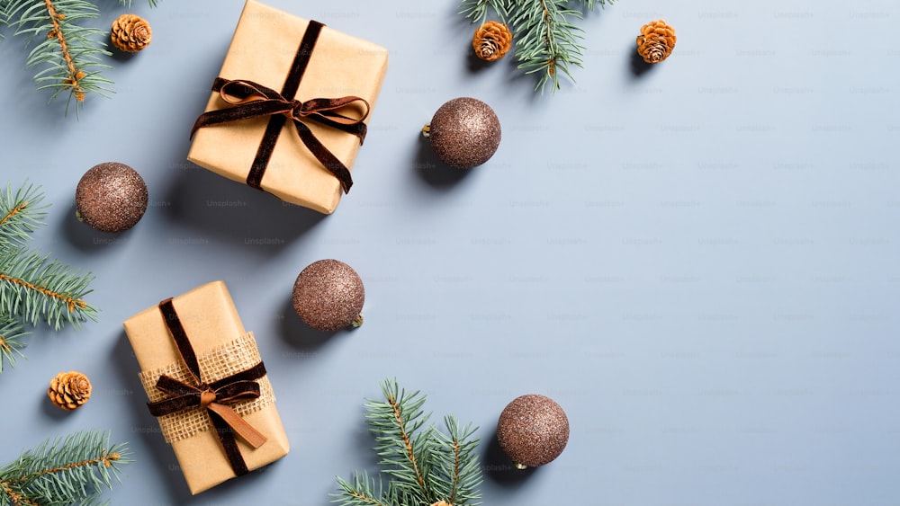 Cajas de regalo de Navidad y bolas marrones con ramas de pino sobre fondo azul pastel. Composición plana navideña de estilo minimalista.