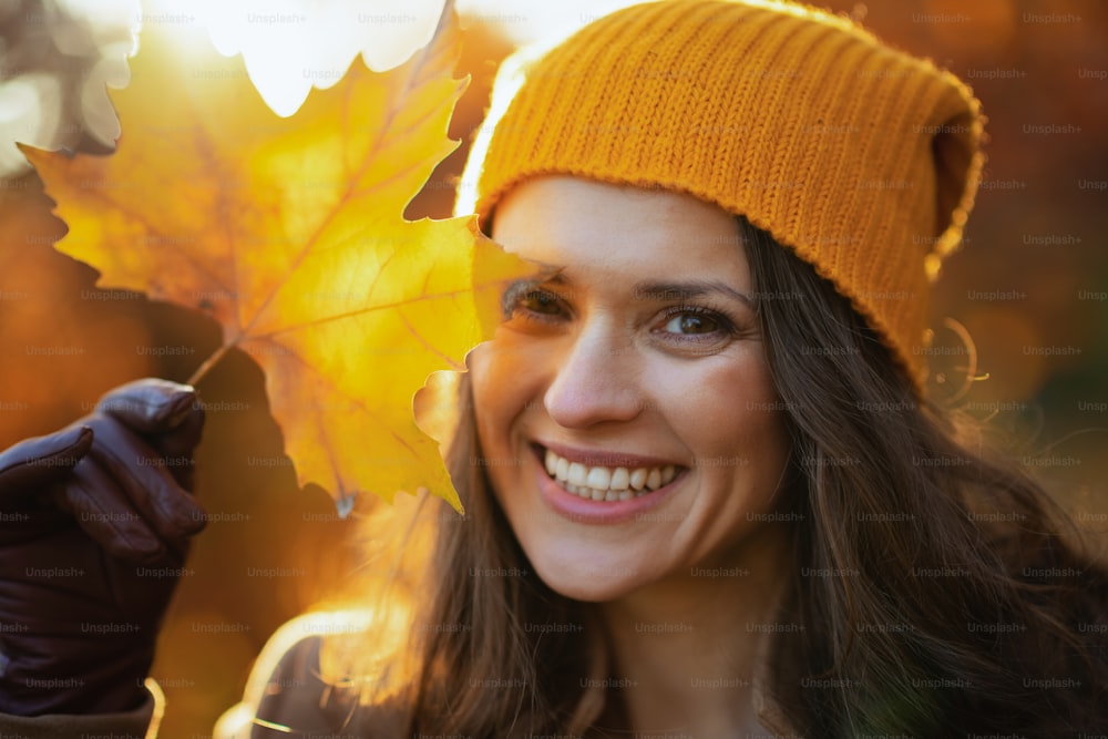 Hello november. smiling stylish woman in brown coat and yellow hat with autumn yellow leaves outdoors in the city park in autumn.