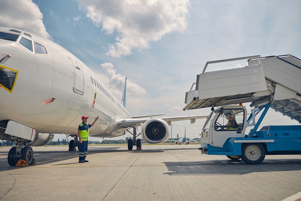 Caucasian aircraft maintenance supervisor in uniform standing in front of a passenger boarding stairs truck