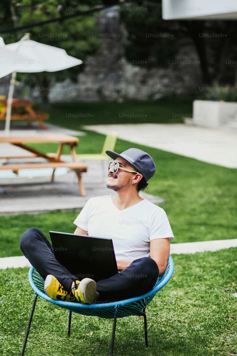 Homem latino trabalhando com laptop ao ar livre em um belo terraço usando smartphone e computador sentado de pernas cruzadas em casa na Cidade do México