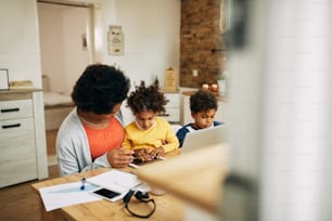 African American mother talking to her daughter while working at home. Small boy is sitting beside them. Copy space.