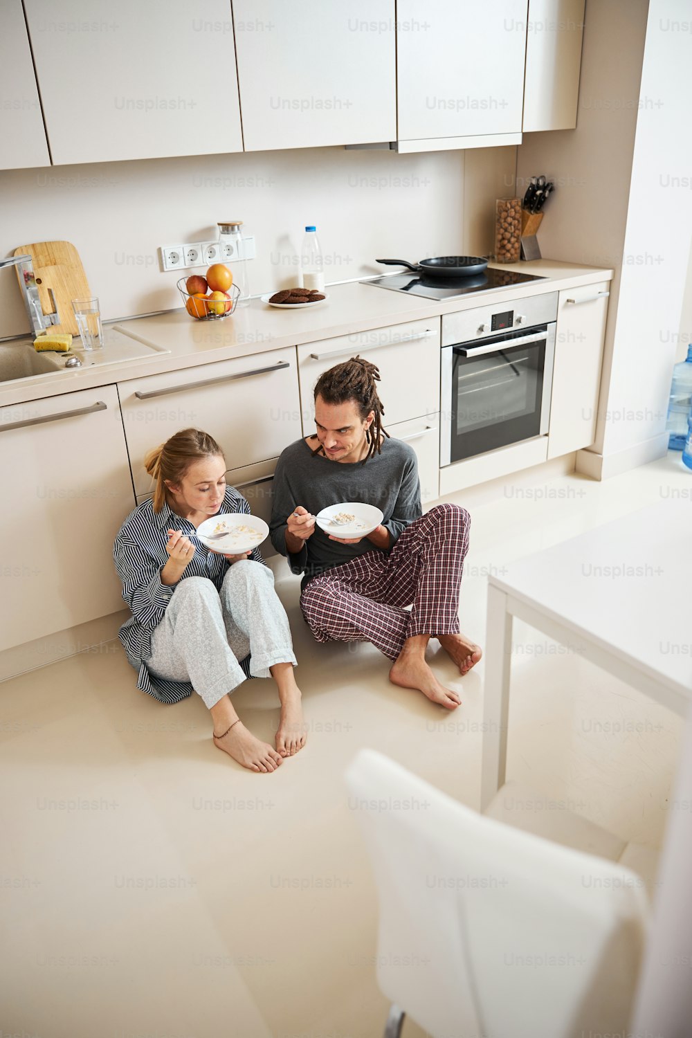 Charming young woman sitting on the floor and eating oatmeal while spending time with boyfriend at home