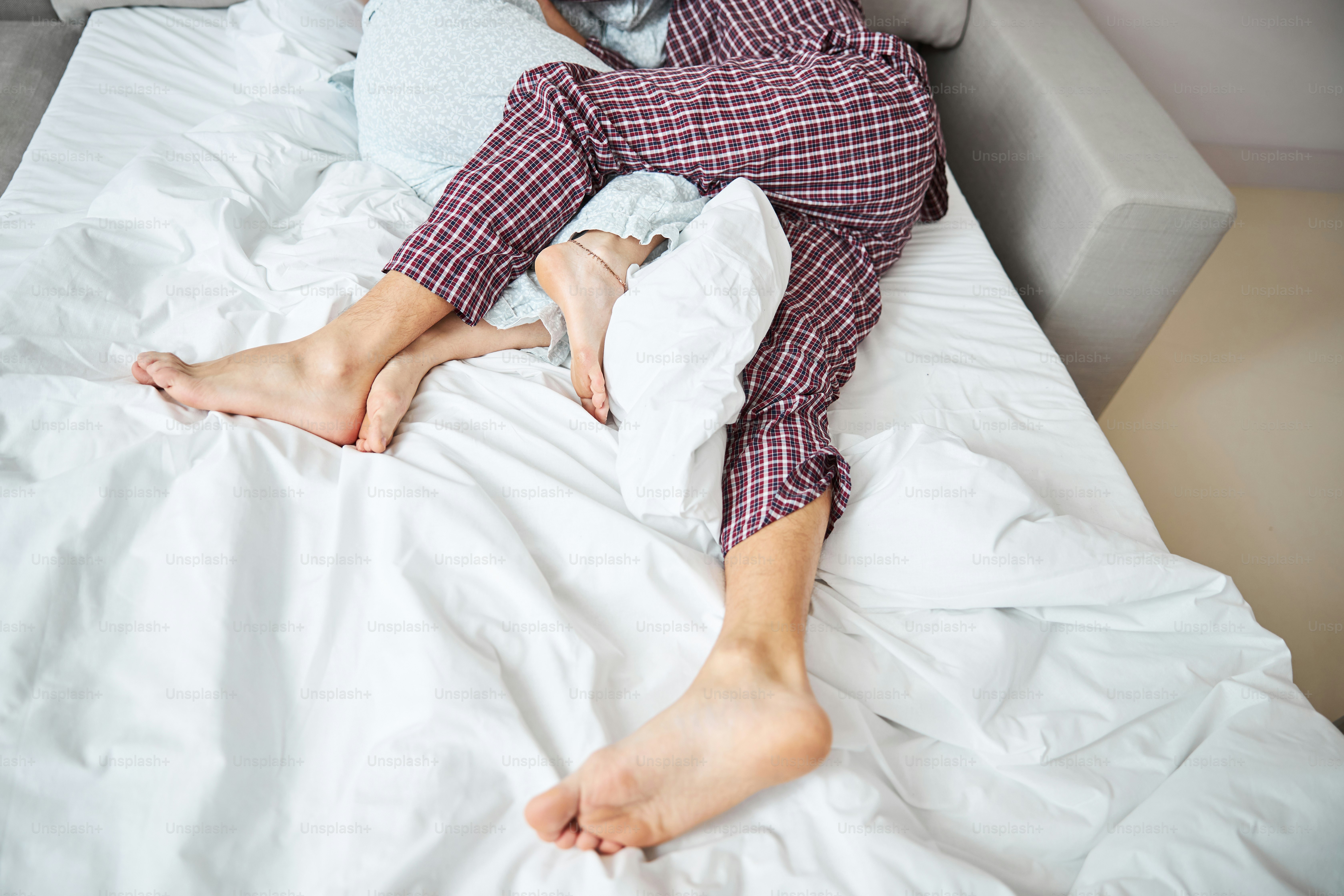 Close up of barefoot man in pajamas hugging girlfriend while resting on ...