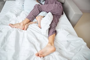 Close up of barefoot man in pajamas hugging girlfriend while resting on white sheets
