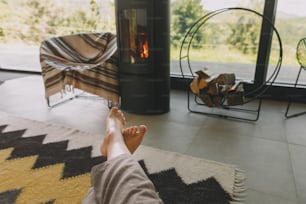 Woman barefoot relaxing in comfortable home, cozy warm moments. Feet on background of modern black fireplace and big windows with view on mountains.