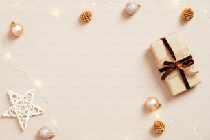 Elegante composizione natalizia. Cornice natalizia composta da confezione regalo, stella, decorazione palline, ghirlanda su sfondo beige pastello. Stile minimale e nordico. Posa piatta.
