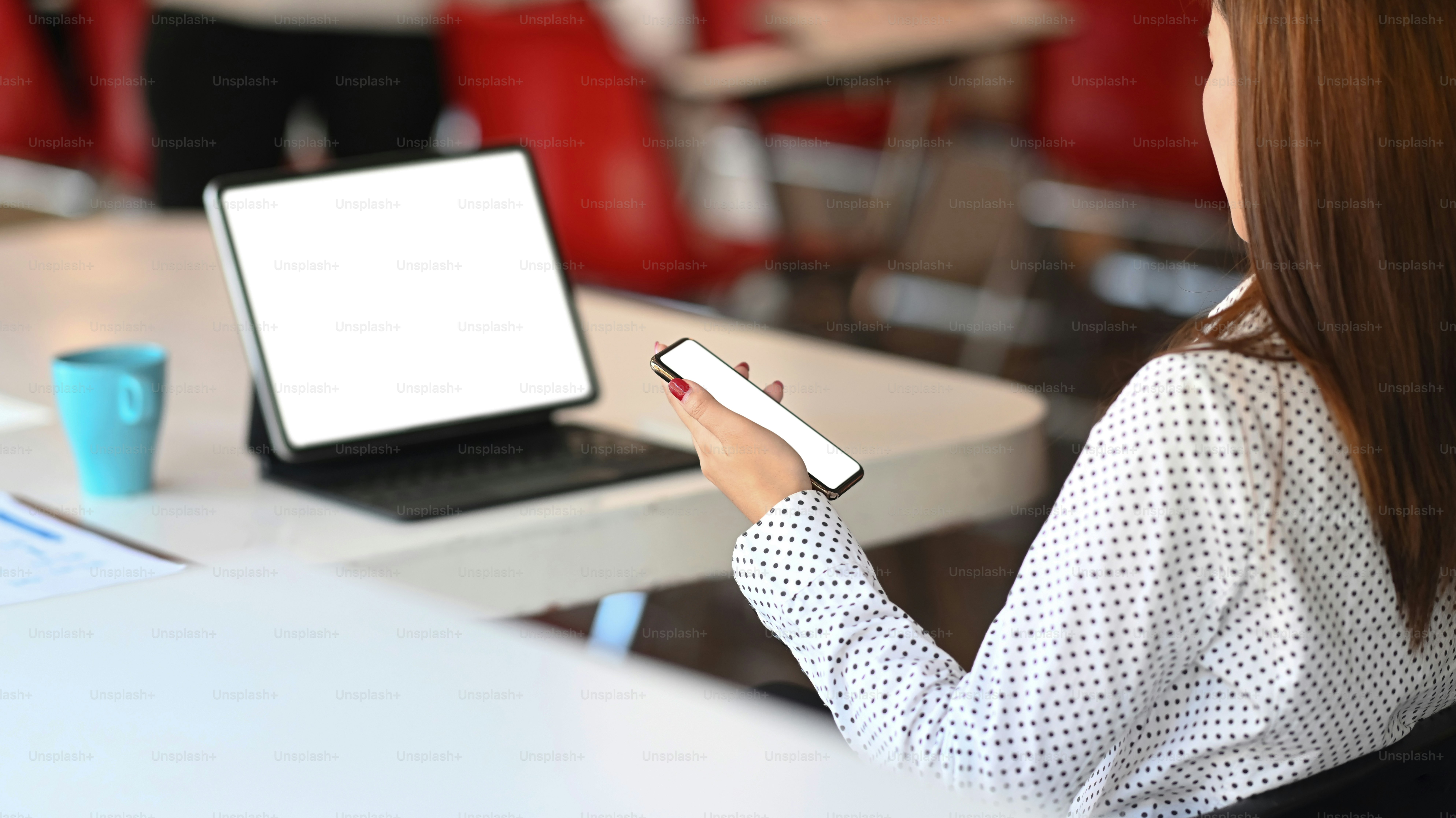 Una mujer joven está sentada frente a una tableta de computadora mientras usa el teléfono móvil. Pantalla en blanco para montaje gráfico.