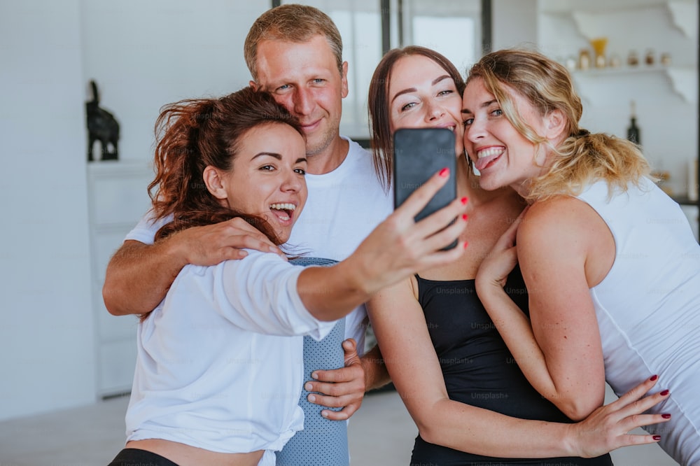 Lächelnde junge Leute, die Spaß daran haben, Selfie-Fotos nach dem Yoga-Kurs drinnen zu machen.