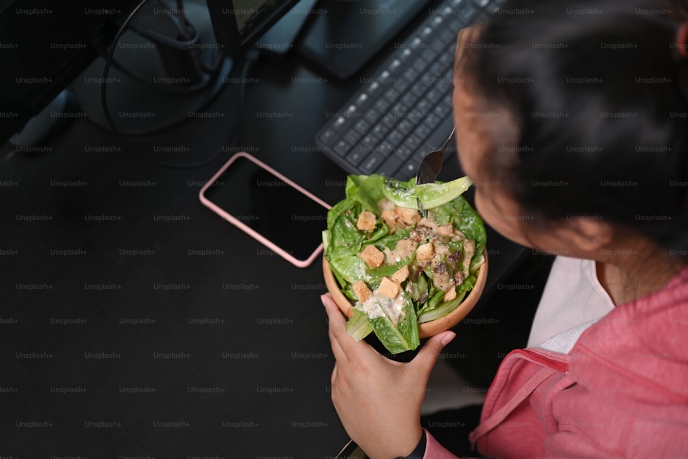 Over head shot of woman overweight having fresh salad at lunch in her workplace.