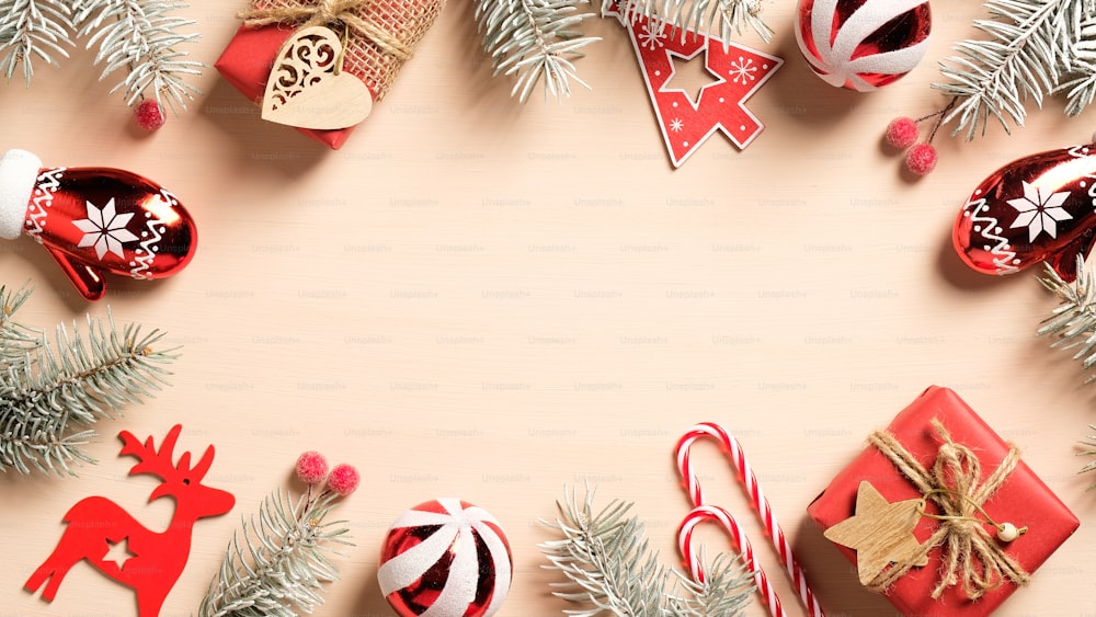 Adornos navideños rojos y cajas de regalo con ramas de abeto sobre fondo beige. Borde de marco de Navidad, plantilla de tarjeta de felicitación de temporada. Plano plano, vista superior, espacio de copia.