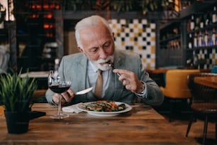 Happy businessman sitting in restaurant and having lunch. He is enjoying in delicious food and wine.