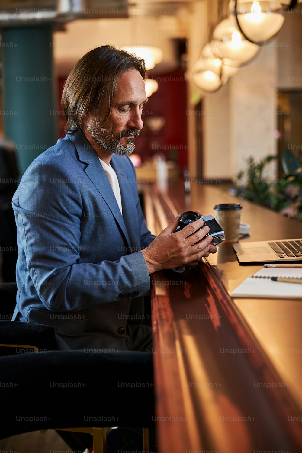 Concentrated man in smart suit looking at his camera lense while sitting alone at a bar counter