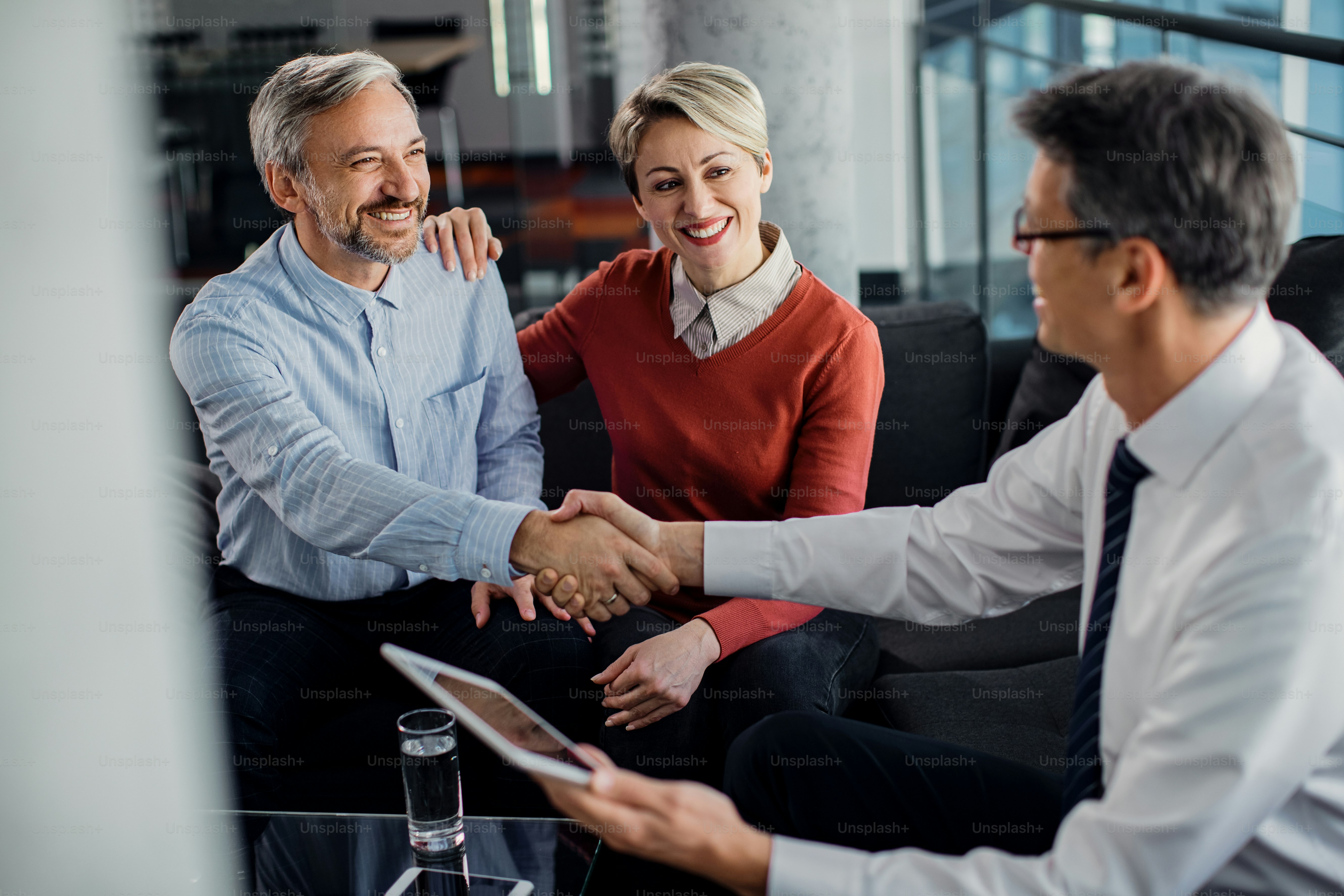 Feliz pareja dándose la mano con el asesor financiero después de una reunión exitosa en la oficina.