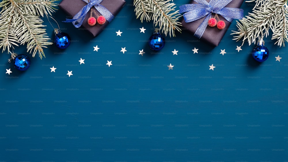 Merry Christmas and Happy Holidays greeting card design with pine tree branches, gift boxes and confetti on dark blue background. Flat lay, top view.