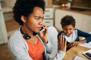 아프리카계 미국인 여성은 집에서 일하는 동안 휴대전화로 통신하고 옆에서 비명을 지르는 아들을 침묵시키려고 합니다.