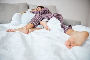 Homme pieds nus en pyjama câlinant sa charmante petite amie tout en faisant une sieste après une longue journée