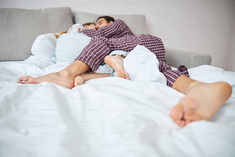 Barfüßiger Mann im Schlafanzug kuschelt mit charmanter Freundin beim Nickerchen nach einem langen Tag