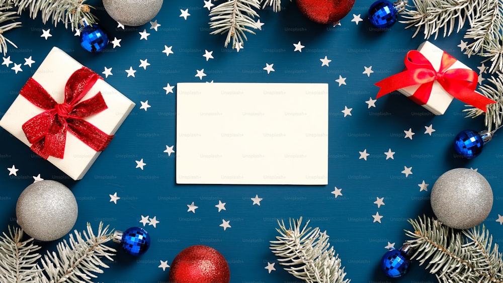 메리 크리스마스 인사말 카드 모형, 빨간 리본 활이 있는 흰색 선물 상자, 소나무 나뭇가지, 진한 파란색 배경에 장식. 플랫 레이, 평면도.