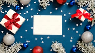 메리 크리스마스 인사말 카드 모형, 빨간 리본 활이 있는 흰색 선물 상자, 소나무 나뭇가지, 진한 파란색 배경에 장식. 플랫 레이, 평면도.