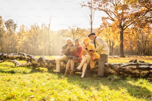 Senioren mit mobilen Smartphones und Tablets im schönen Herbstpark. Freunde im Ruhestand, die Zeit im Freien miteinander verbringen.