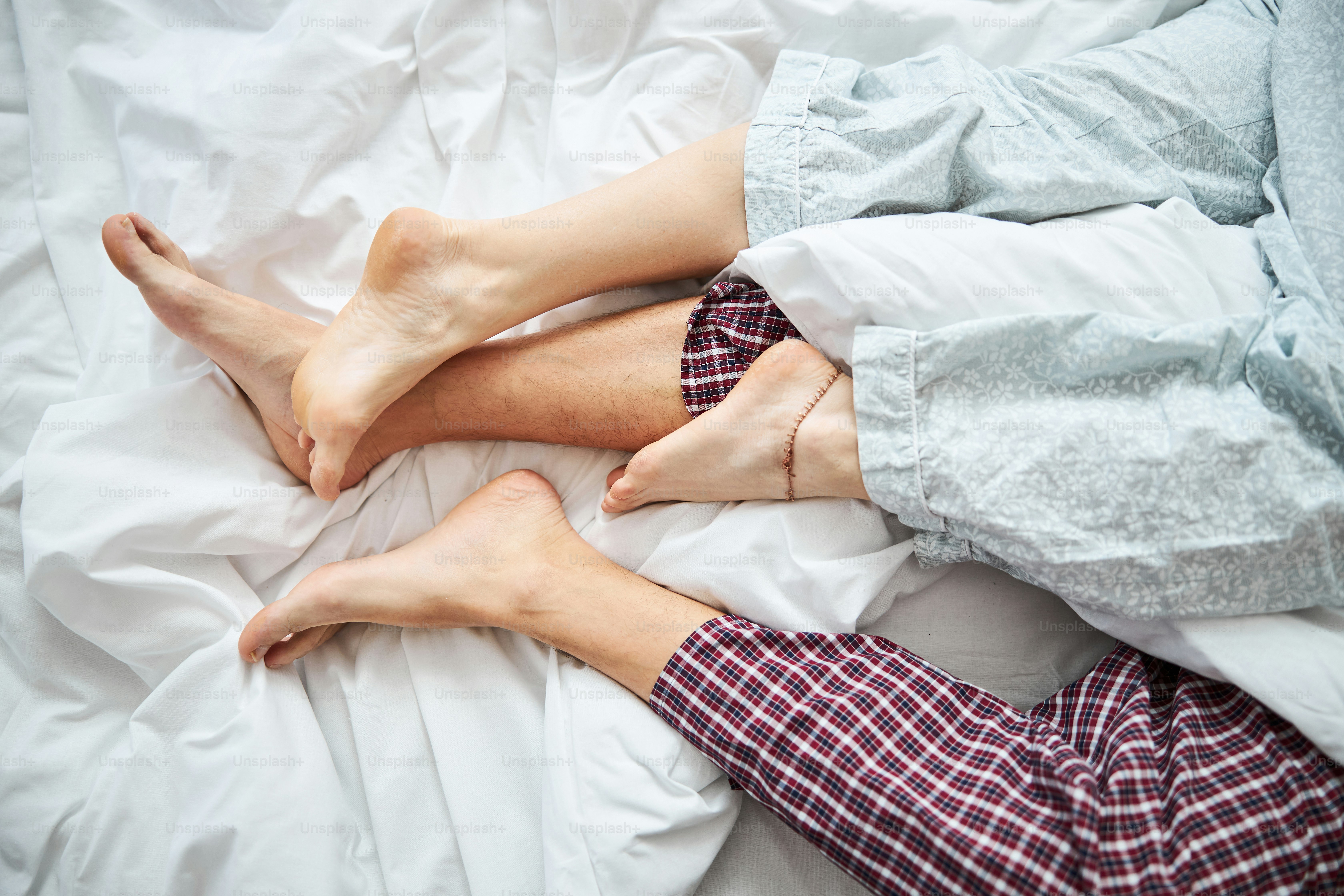 Close up of barefoot boyfriend and girlfriend sleeping together on white sheets