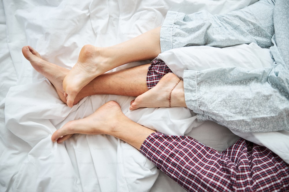 Close up of barefoot boyfriend and girlfriend sleeping together on white sheets