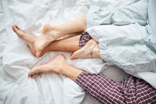 Close up of barefoot boyfriend and girlfriend sleeping together on white sheets