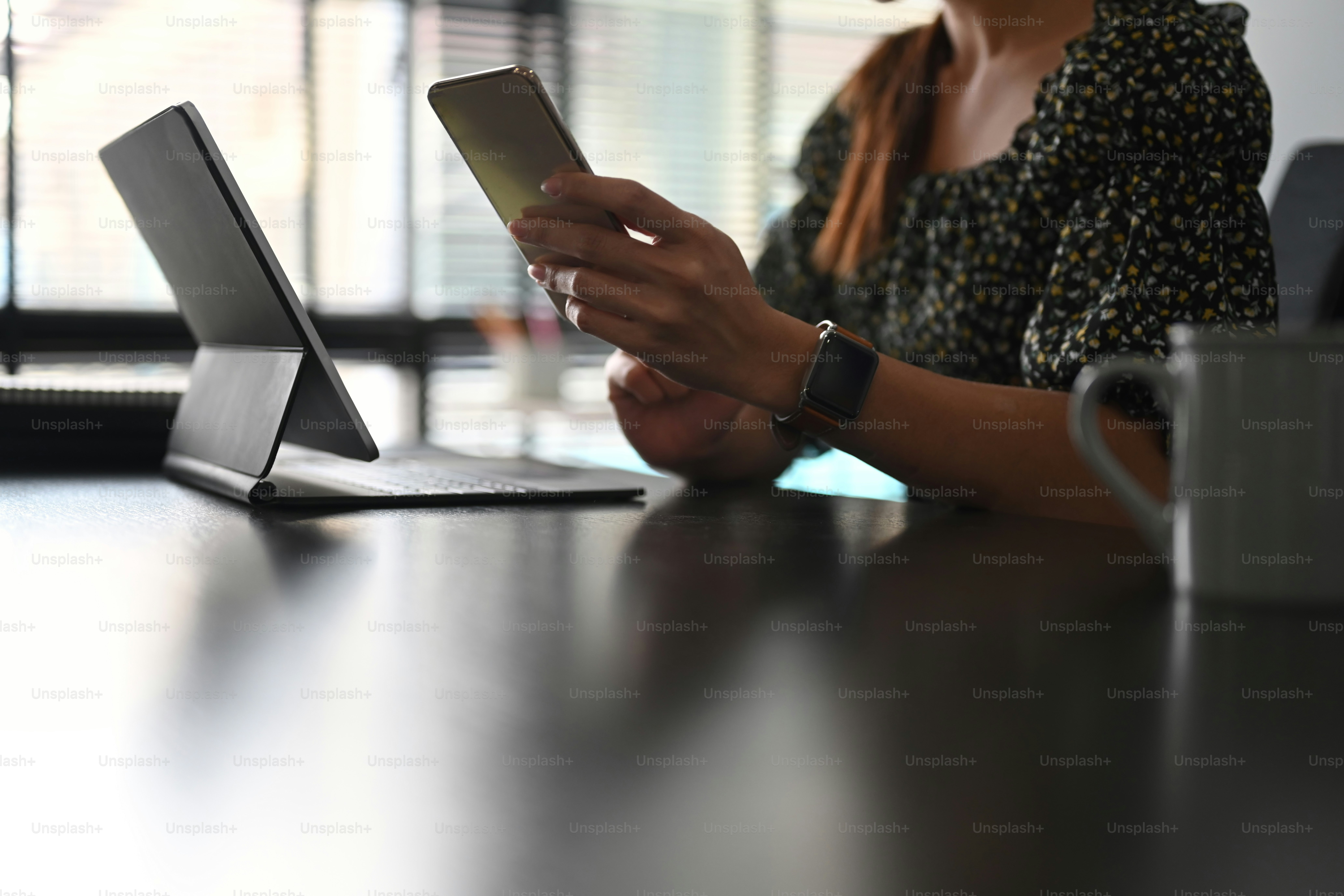 Foto recortada: una mujer independiente está usando un teléfono móvil mientras trabaja en una tableta de computadora en la sala de oficina.